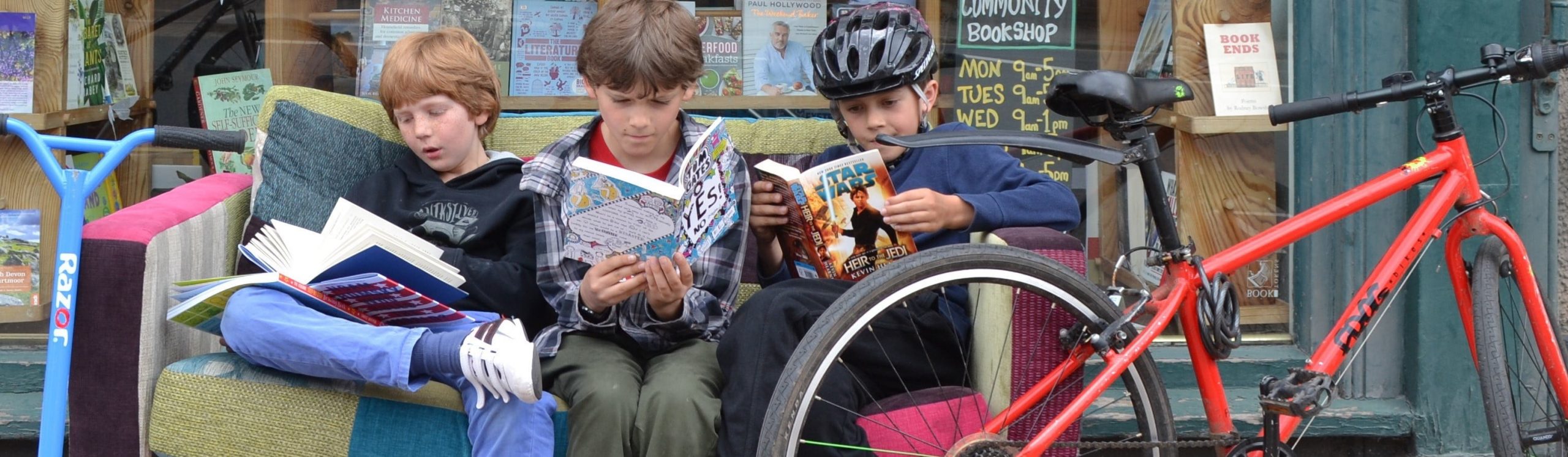 Boys sat on sofa outside bookshop reading books